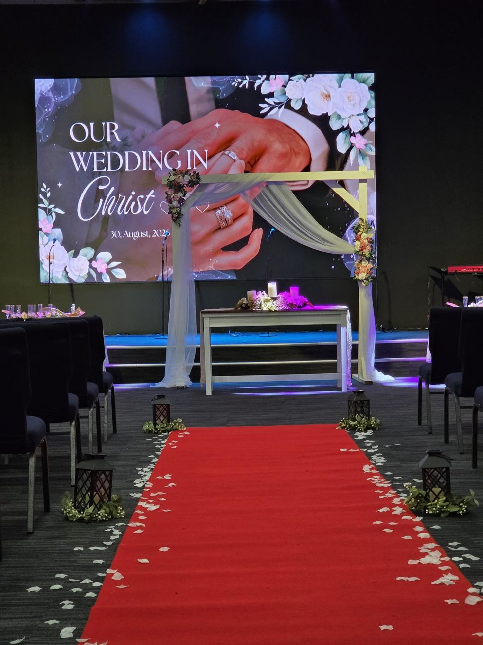 Red aisle runner with lanterns and petals in front of the arch